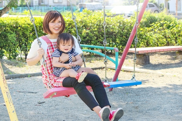 保育士と子供がブランコで遊んでいる画像